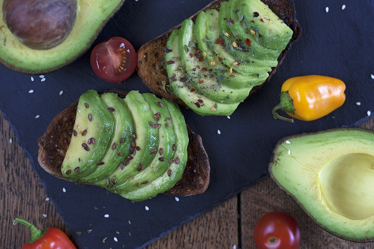 Sliced avocado on seeded sourdough with cherry tomato and peppers on a slate board