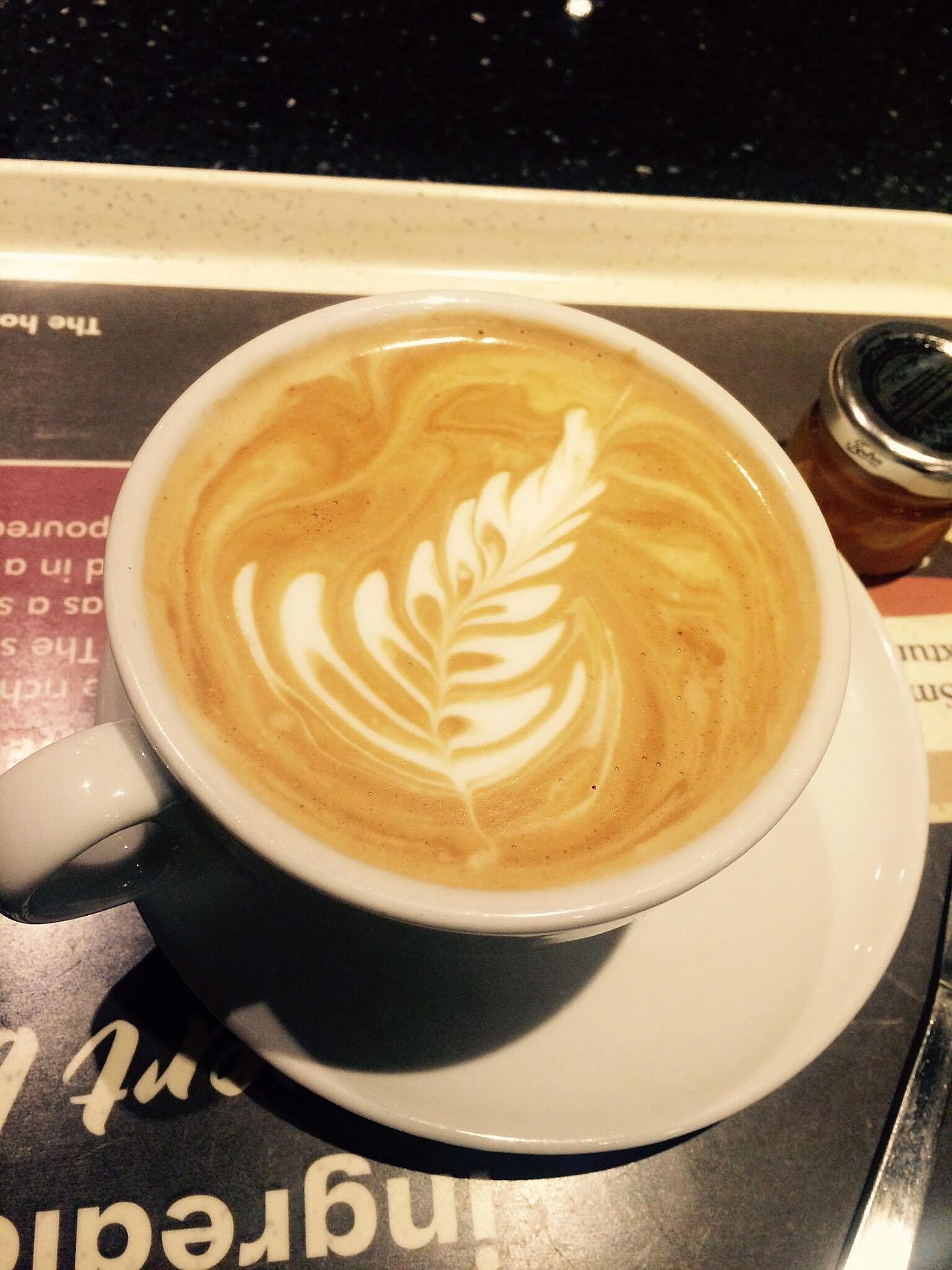 Flat white coffee in a white cup with a feather pattern in the milk
